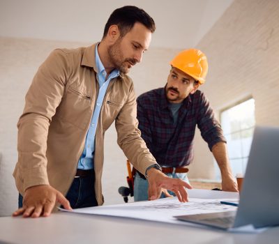 Home owner analyzing blueprints with a worker during renovation process.