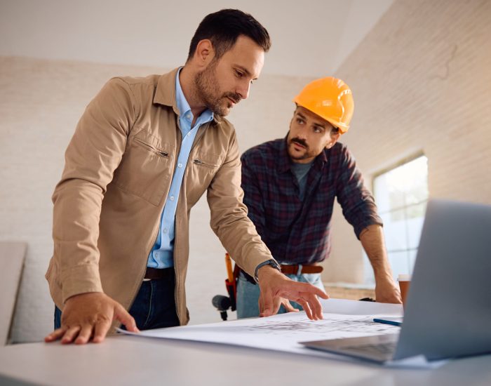 Home owner analyzing blueprints with a worker during renovation process.